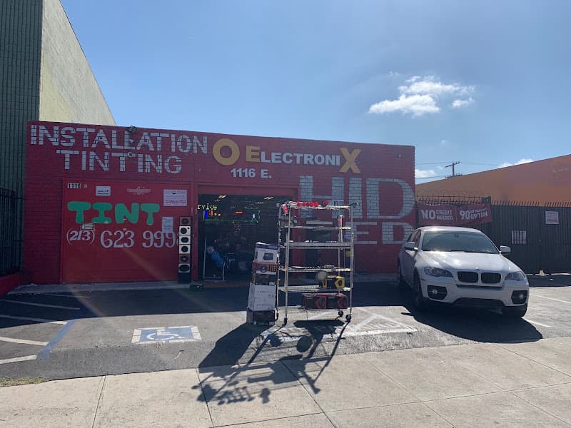 Red brick storefront with tint signs and a white SUV parked out front at O Electronix Inc. in Los Angeles, California