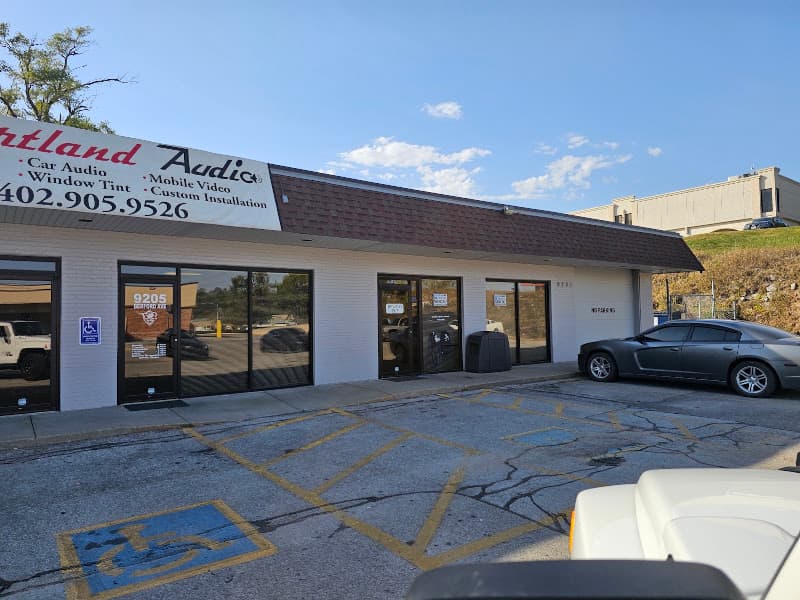 Storefront with glass entry doors and a gray sedan parked outside at Heartland Audio in Omaha, Nebraska