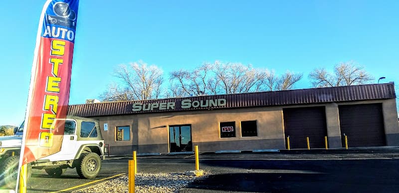 Stucco building with metal roof, two garage doors and AUTO STEREO flag at SUPER SOUND in Santa Fe, New Mexico