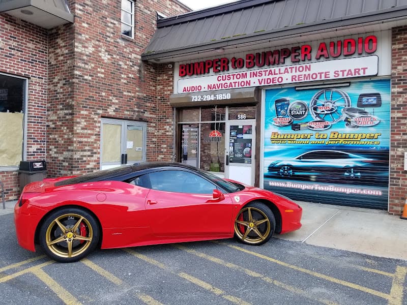 Red sports car parked in front of a brick storefront at Bumper to Bumper Car Audio in Freehold, New Jersey