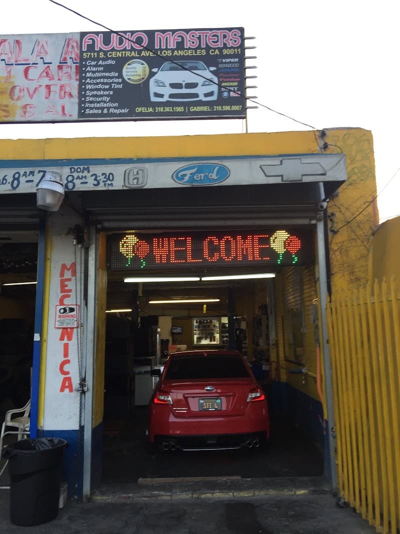 Shop bay with red sedan inside, LED welcome sign overhead at Audio Masters in Los Angeles, California