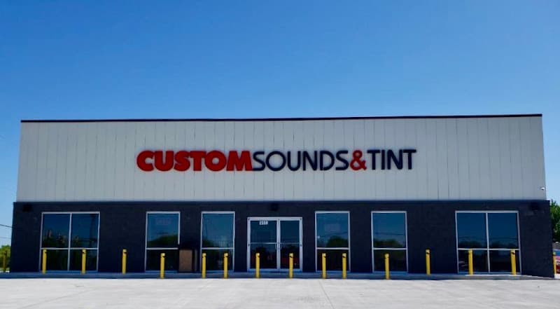Storefront with red and black sign and yellow bollards at Custom Sounds & Tint - Norman OK in Norman, Oklahoma