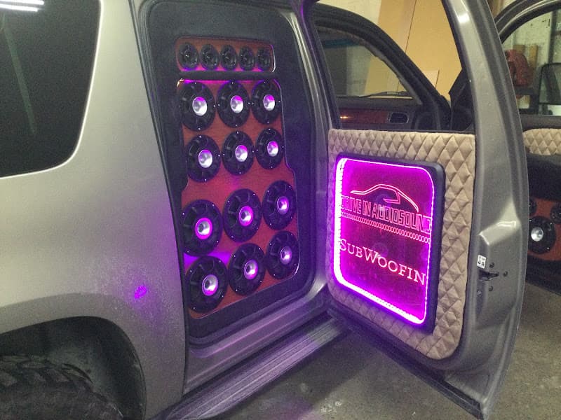 Open SUV door with lit subwoofer panel and purple LED sign at Drive In Audiosound LLC in Midvale, Utah