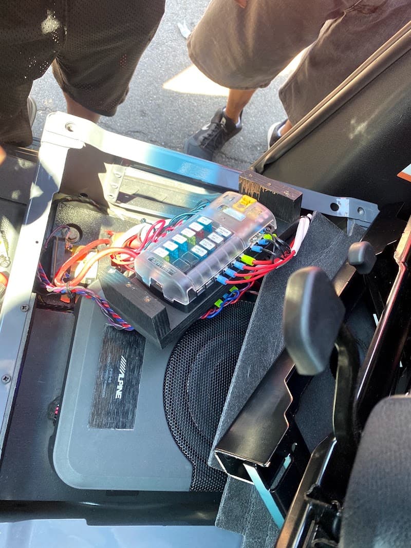 Fuse block and wiring above a black Alpine-labeled unit under a seat at Platinum Audio in Junction City, Kansas