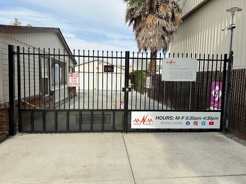 Black iron driveway gate with hours sign and red logo sign at MnM Mobile Solutions in San Jose, California