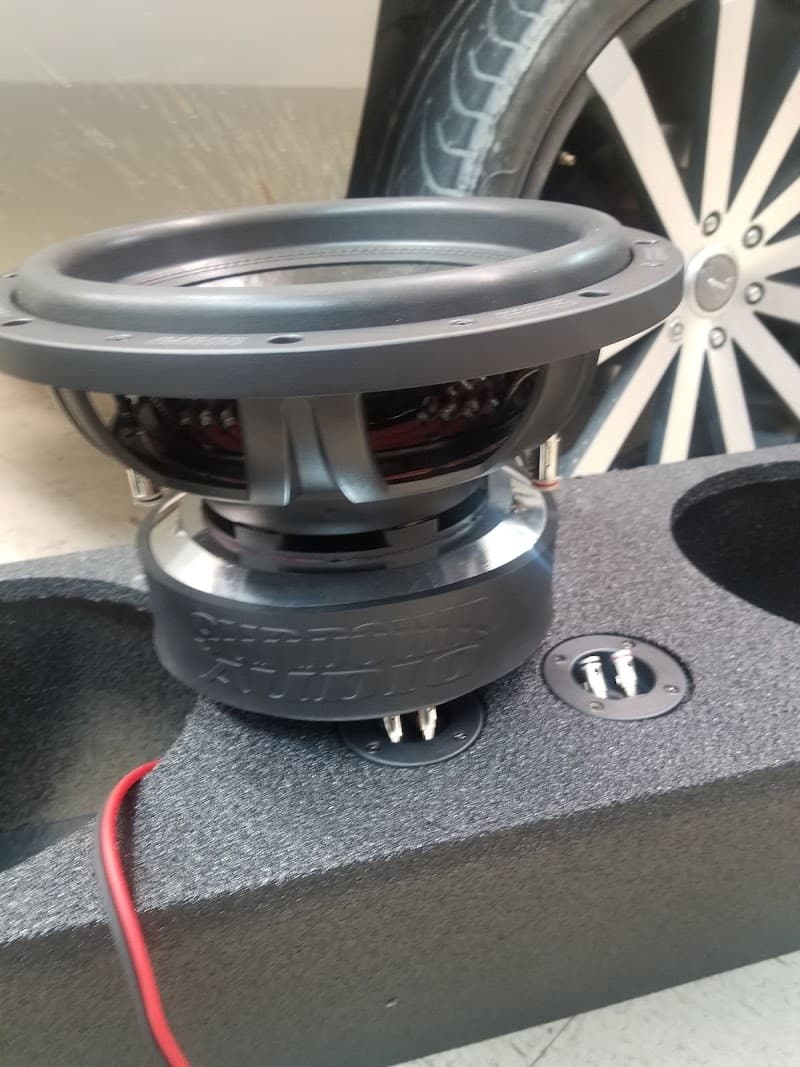 Subwoofer on a carpeted speaker box with a chrome wheel behind at T town Audio in Tulsa, Oklahoma