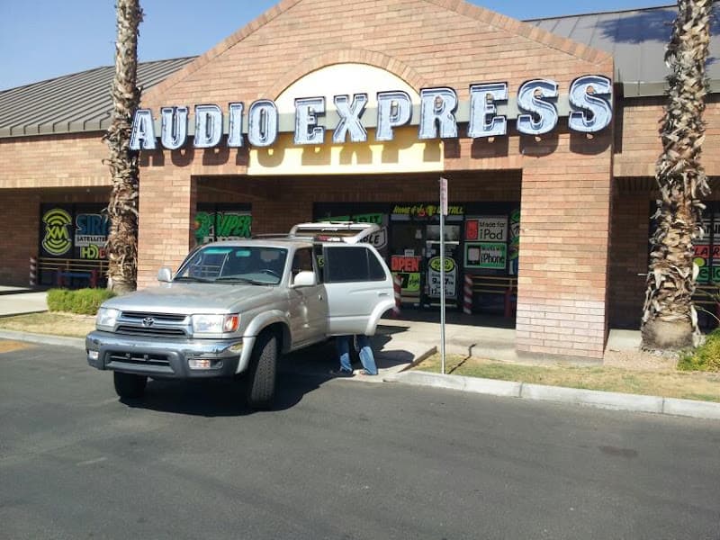 Silver SUV with open door parked outside brick storefront at Audio Express in Mesa, Arizona