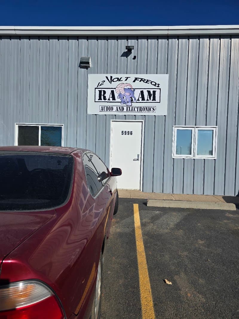 Gray metal storefront with ram logo and red sedan outside at Raam Audio and Electronics in Colorado Springs, Colorado
