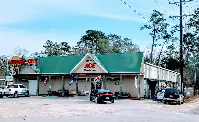 Green-roofed storefront with parked cars and a red and yellow sign at Mobile One Auto Sound in Covington, Louisiana