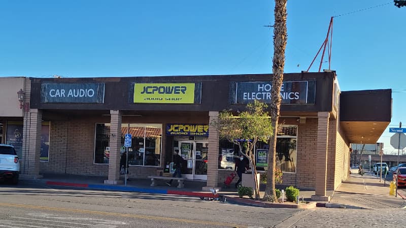 Storefront with yellow sign and tall palm tree out front at JC Power Audio Shop Calexico in Calexico, California