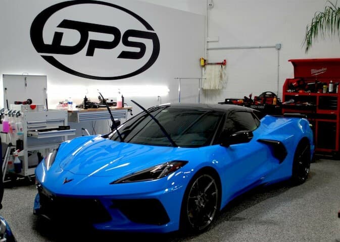Blue sports coupe parked under a black logo sign at DPS Automotive in Arlington Heights, Illinois