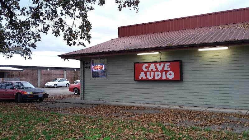 Storefront with red sign on gray siding and parked cars at Cave Audio in Woodburn, Oregon