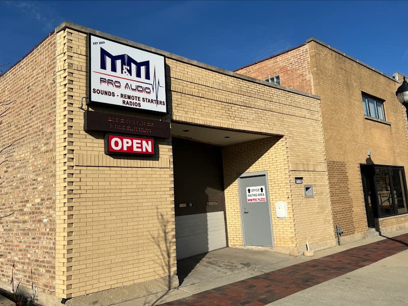 Tan brick storefront with a logo sign and red OPEN sign at M&M Pro Audio in River Grove, Illinois