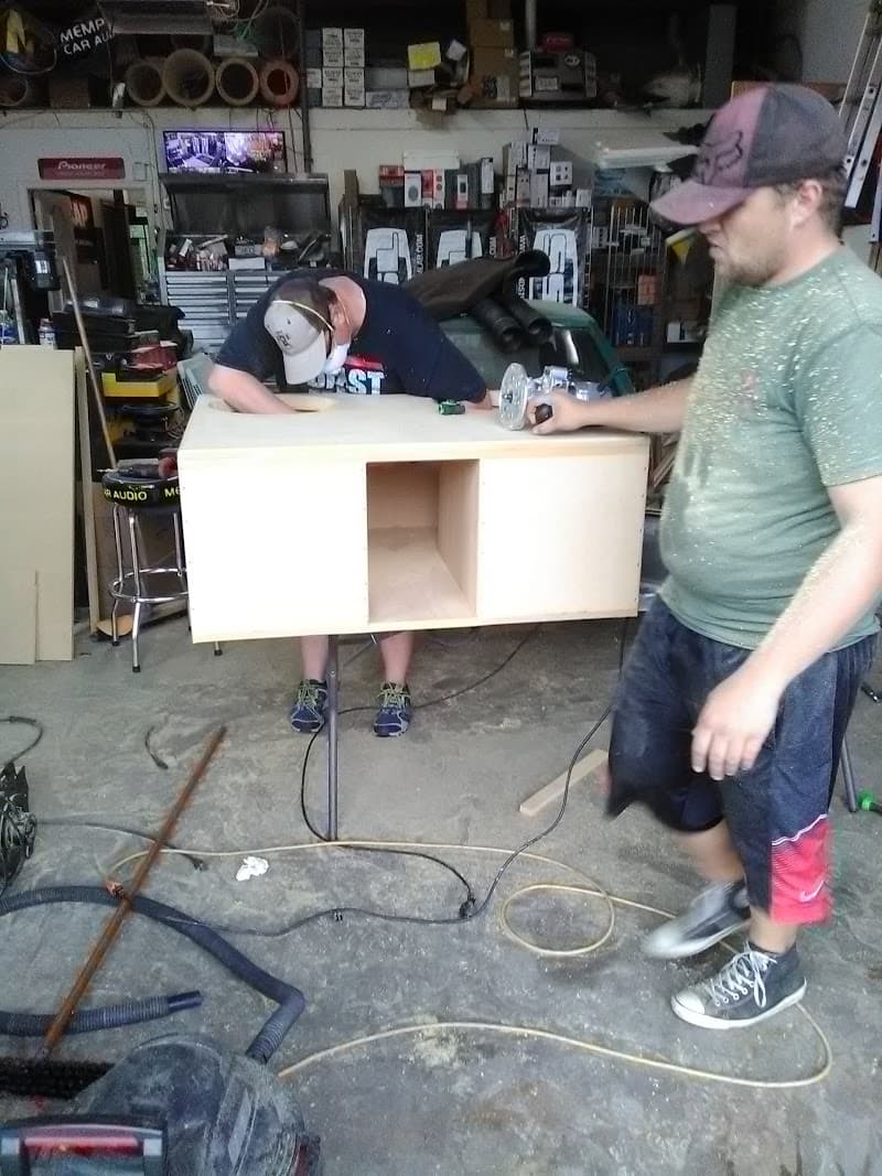 Two men building a wood subwoofer enclosure in a garage at Performance Audio in Enid, Oklahoma