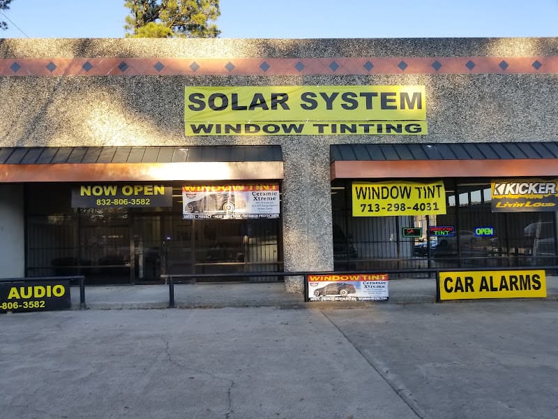 Storefront with yellow window tint and car alarm signs at Solar System Auto Accessories in Houston, Texas