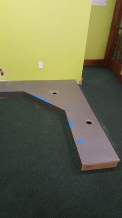 Gray platform with two round cutouts and blue tape marks on green carpet at Crazy Car Audio in College Park, Maryland