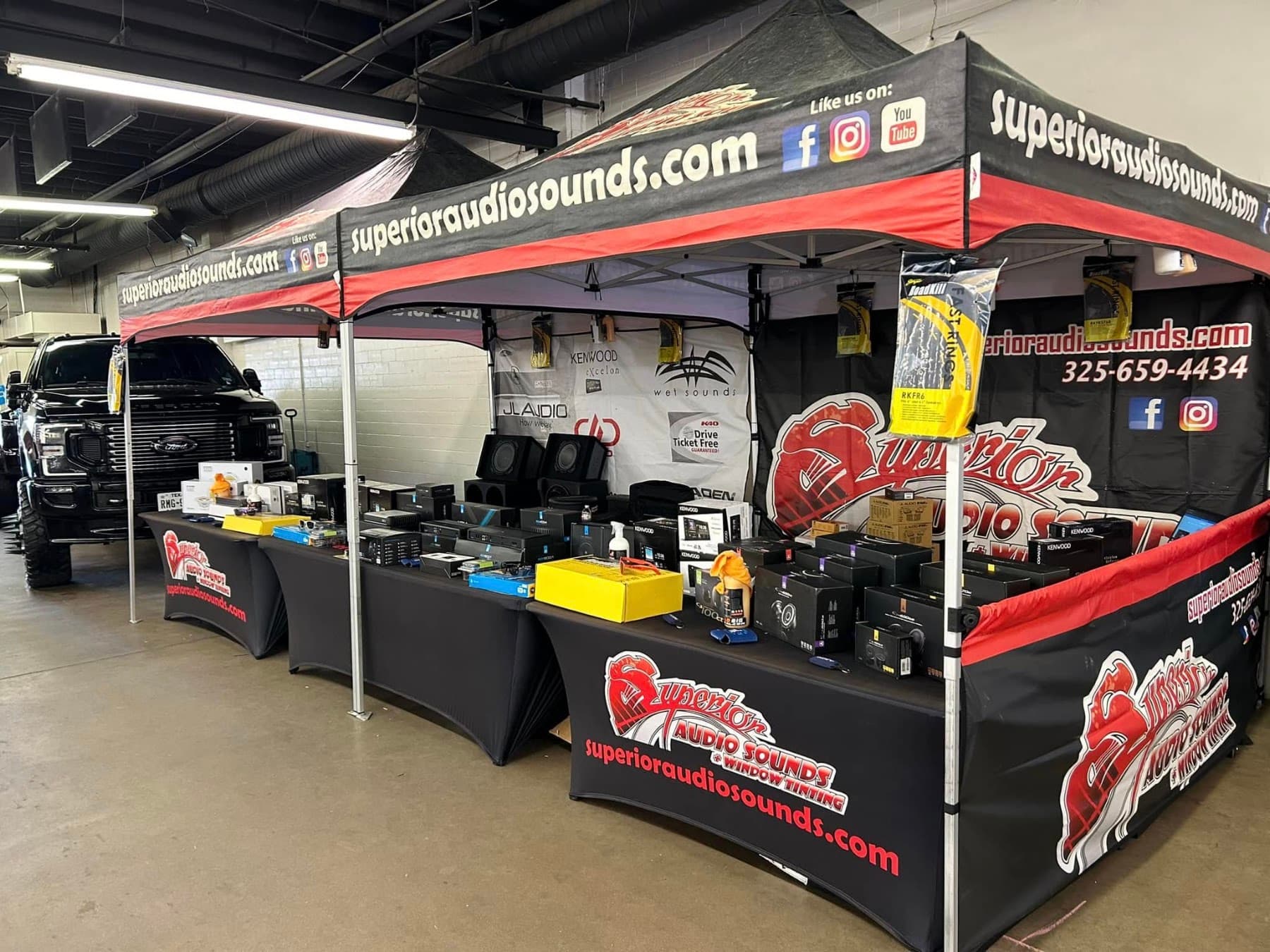 Pop-up booth with car audio products and a black Ford pickup at Superior Audio Sounds in San Angelo, Texas