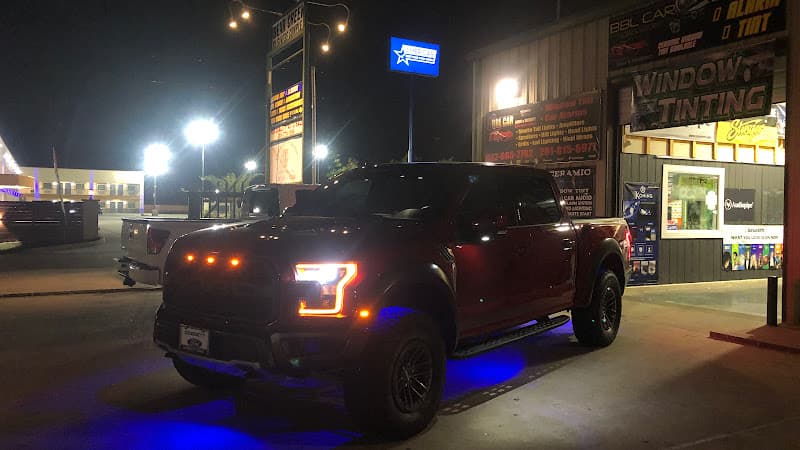 Red pickup truck with blue underglow lights parked outside shop at BBL CAR AUDIO AND SECURITY in Houston, Texas
