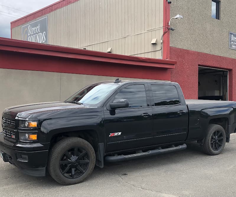 Black pickup truck parked beside a red and tan building at Street Sounds in Fairbanks, Alaska