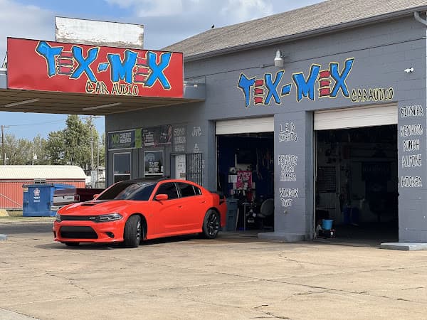 Red sedan parked in front of gray shop with red sign at Tex-Mex Car Audio in Oklahoma City, Oklahoma