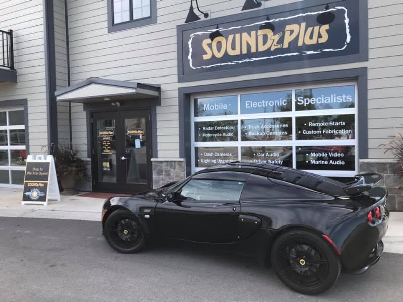 Black sports car parked outside a storefront with window signs at Soundz Plus in Naperville, Illinois