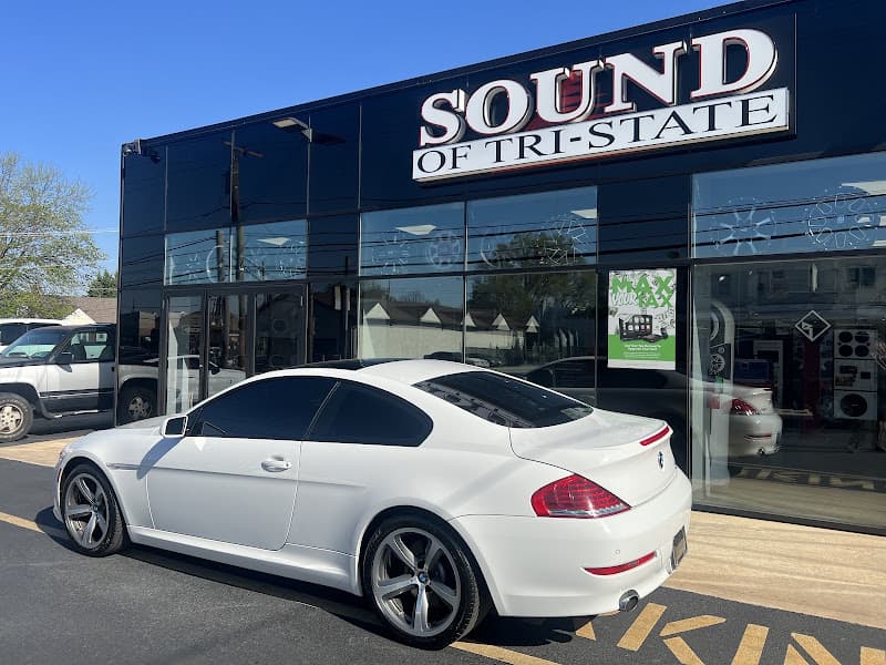 White coupe parked outside a glass storefront with a large sign at Sound of Tri-State in Folsom, Pennsylvania