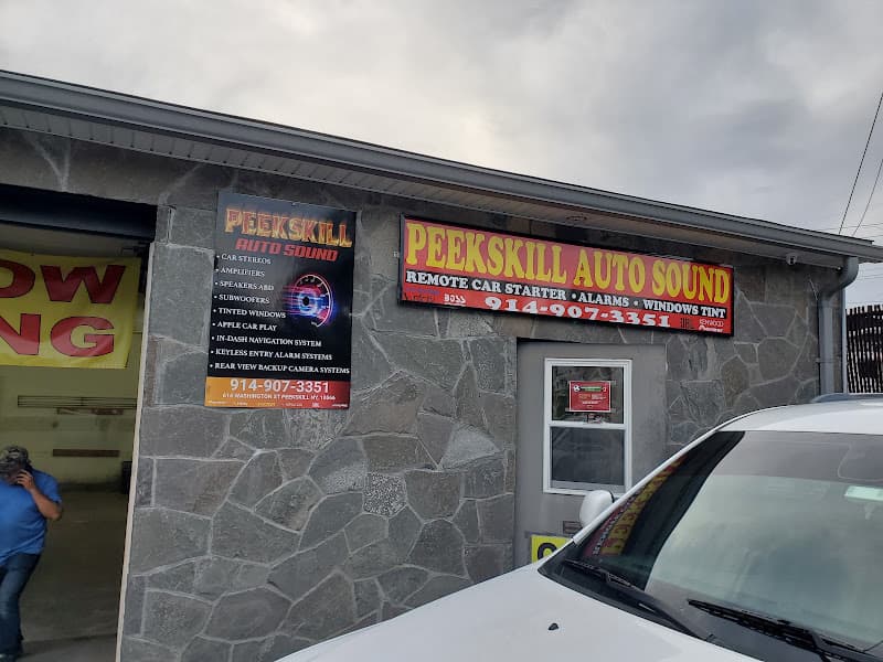 Stone storefront with open garage bay and a man on the phone at Peekskill Auto Sound in Peekskill, New York