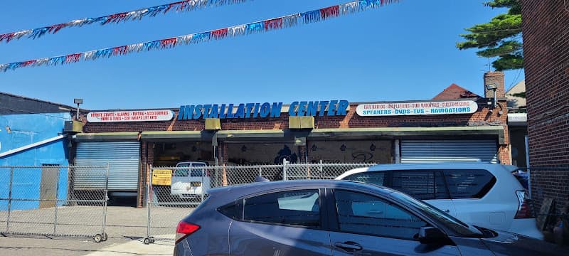 Brick storefront with a blue and red sign and parked cars at Brooklyn Car Audio in Brooklyn, New York