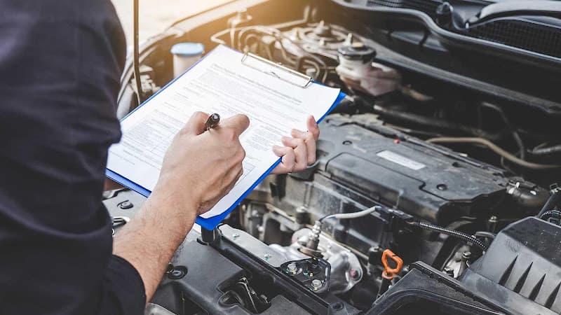 Person writing on a clipboard beside an open car engine at Car Tunes & More in New Bedford, Massachusetts