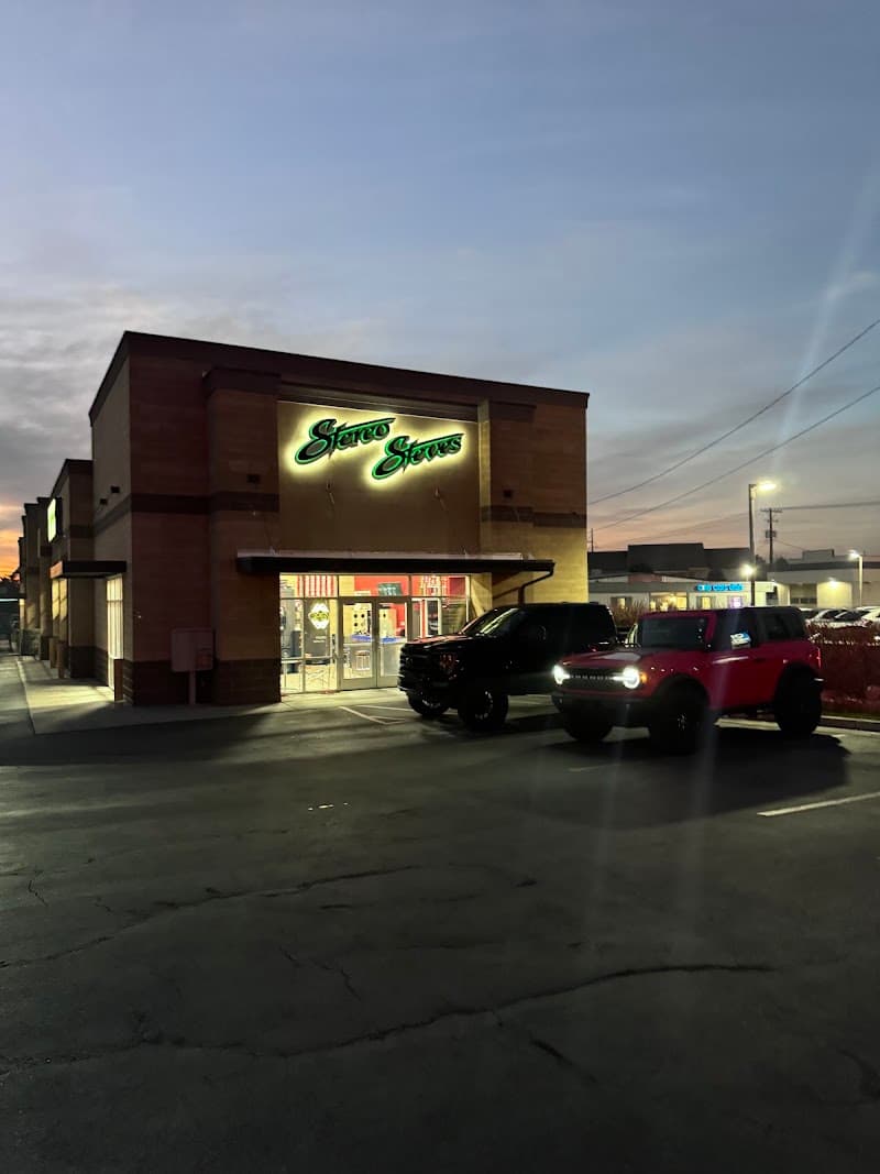 Storefront with green neon sign and two parked vehicles at Stereo Steve's in Orem, Utah