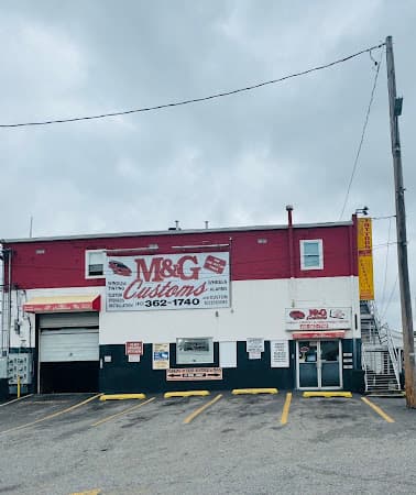 Storefront with red and white facade and roll-up bay door at M & G Customs in Baltimore, Maryland