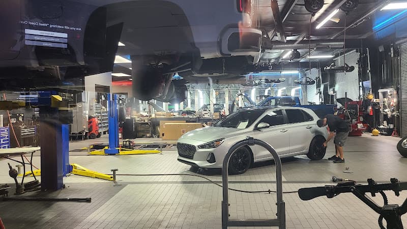 Silver hatchback in a shop bay with a man working on its wheel at BadAss Rides LLC in Fort Myers, Florida