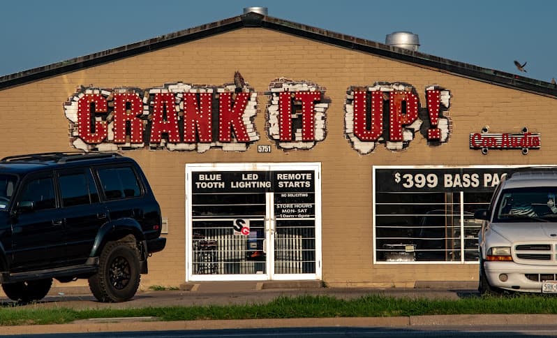 Tan brick storefront with red-lit sign and parked SUV at Crank It Up Car Audio in North Richland Hills, Texas