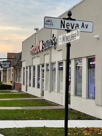 Storefront with red sign beside Neva Av and Milwaukee Av street signs at Armando Sounds in Niles, Illinois