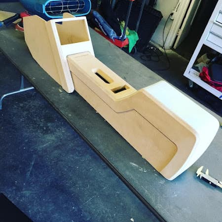Unfinished wooden center console with white-painted ends on a workbench at 290 Car Audio in Cypress, Texas