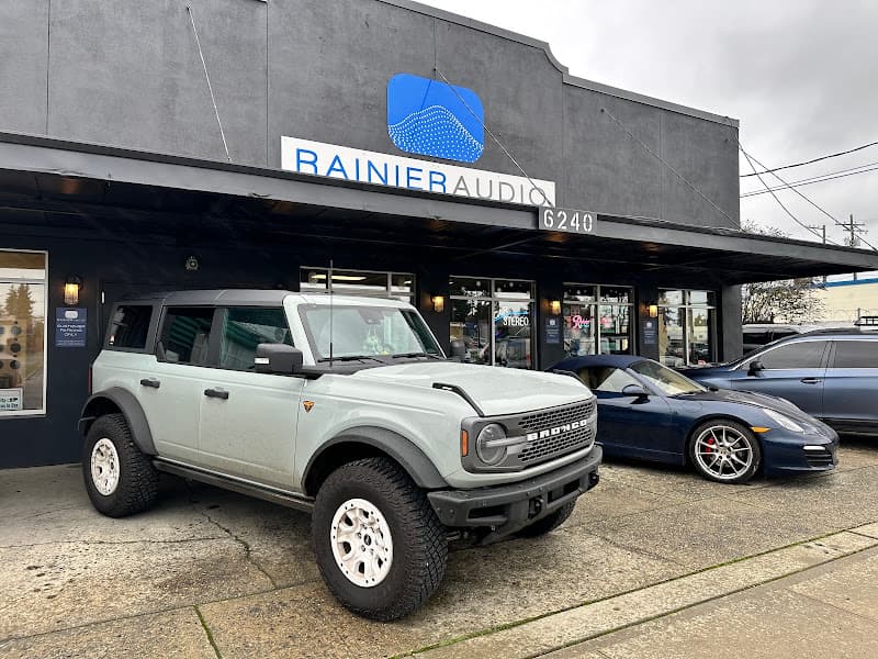 Gray Bronco SUV and dark sports car parked outside storefront at Rainier Audio in Tacoma, Washington