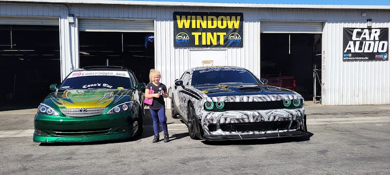 Woman between a green sedan and a muscle car at Active Sound & Alarms Car Stereo Shop in San Jacinto, California