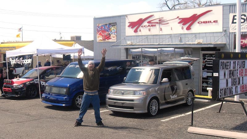 Man with arms raised beside parked cars outside a shop at McCain Audio in Farmington, New Mexico