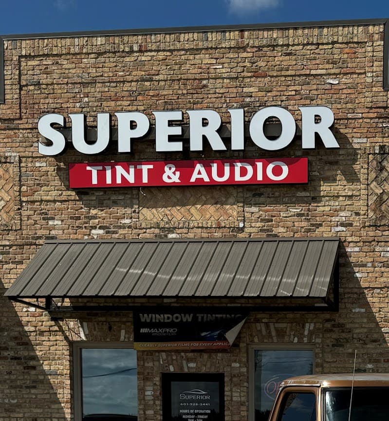 Brick storefront with white and red sign and metal awning at Superior Tint & Audio in Wiggins, Mississippi