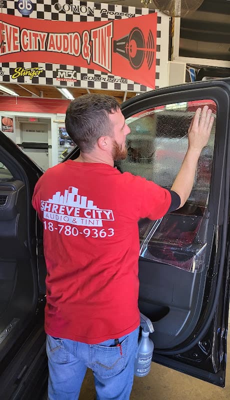 Technician in red shirt applying tint to an SUV window at Shreve City Audio & Tint in Shreveport, Louisiana