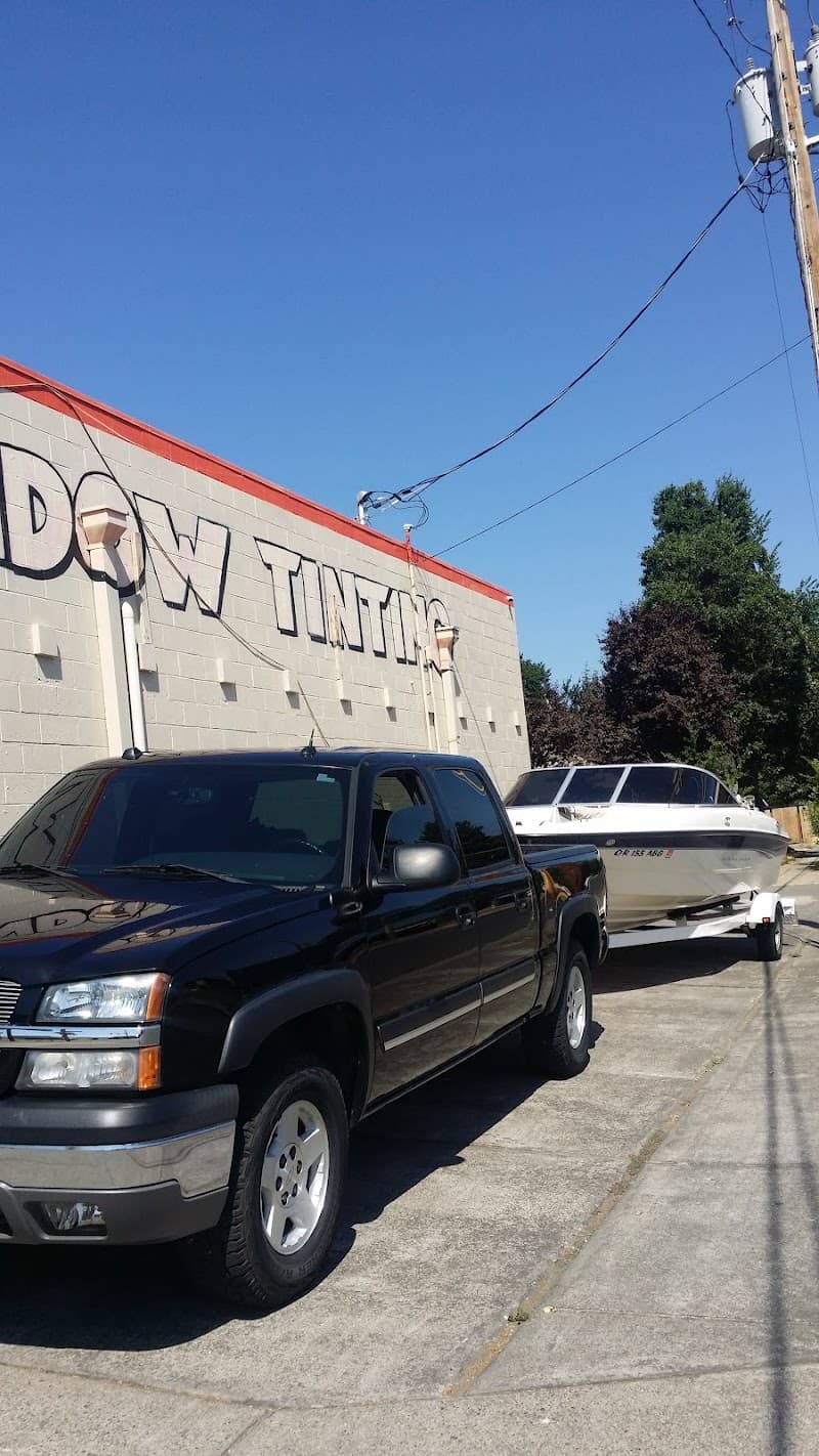 Black pickup truck towing a white boat beside a tinting shop wall at Sport Audio in Medford, Oregon
