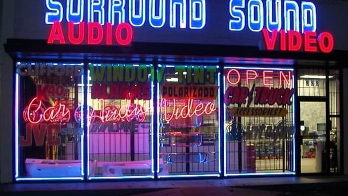 Neon-lit storefront with window signs and an open sign at Surround Sound in Richardson, Texas