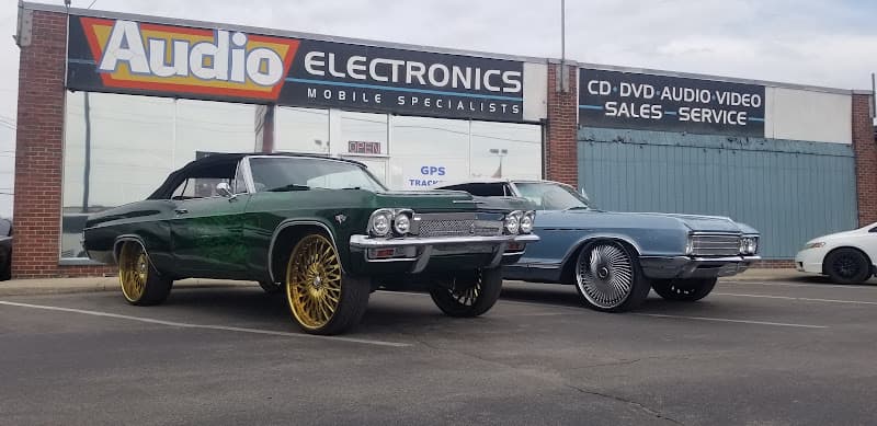 Green and blue classic cars parked outside storefront at Audio Electronics in Indianapolis, Indiana