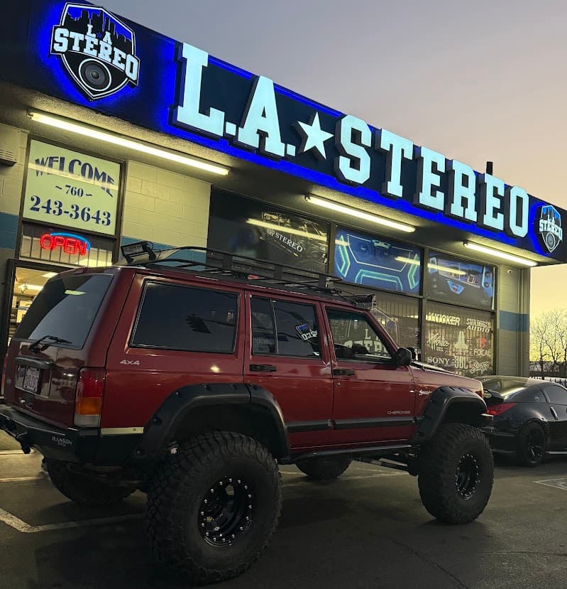 Red lifted SUV with Cherokee badge parked outside storefront at L.A Stereo & window tint in Victorville, California