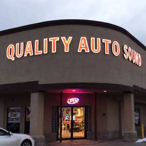 Storefront with lit orange sign above the entrance at Quality Auto Sound in Lakewood, Colorado