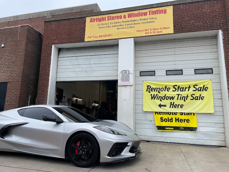Silver sports car beside a garage with sale signs at Airtight Stereo & Window Tinting Service in Hartford, Connecticut