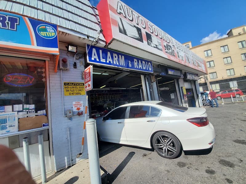 Storefront with Alarm & Radio sign and white car inside at Auto Sound & Security Accessories in Jamaica, New York