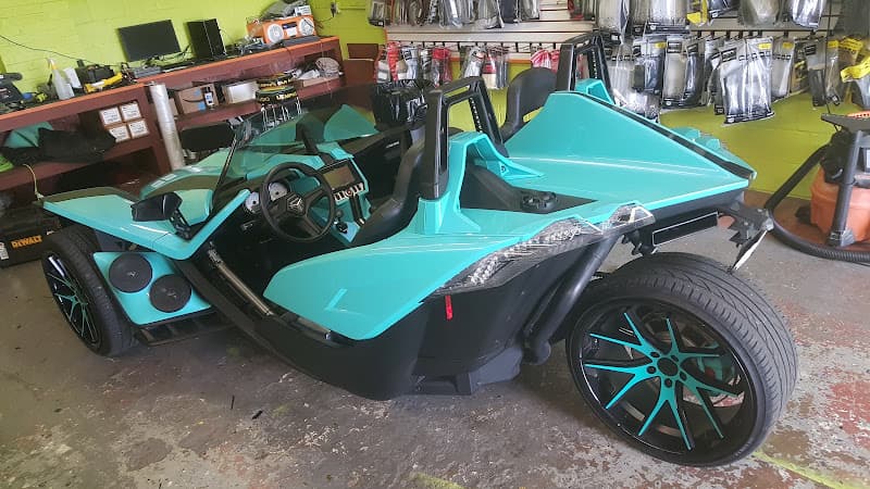 Turquoise three-wheeled roadster with black wheels in a shop bay at Crazy Car Audio in College Park, Maryland