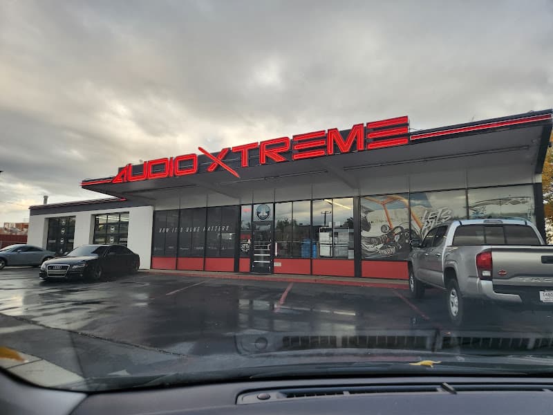 Storefront with red logo sign, parked pickup truck and sedan at Audio Xtreme Sound & Security in Ogden, Utah