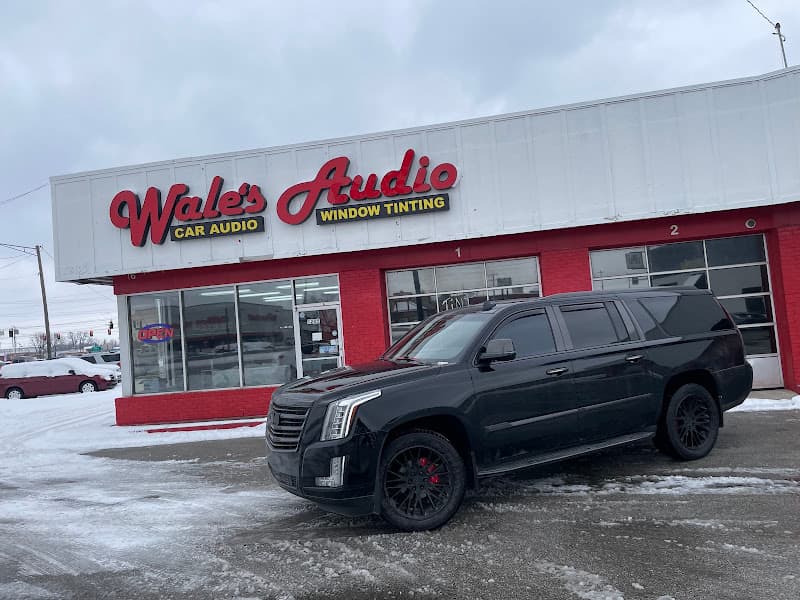 Black SUV parked outside a storefront with red script signs at Wale's Audio and Window Tinting in Greenwood, Indiana
